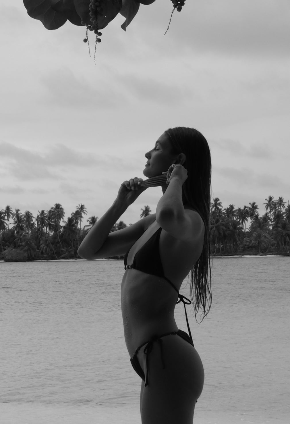 Woman using a ma·ru facial sculpting roller along the jawline in a tropical coastal setting, supporting facial massage, lymphatic drainage, de-puffing, muscle stimulation and a more sculpted, refreshed-looking complexion.